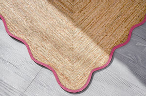 Handwoven natural jute scalloped area rug with elegant pink border for modern boho living room decor.