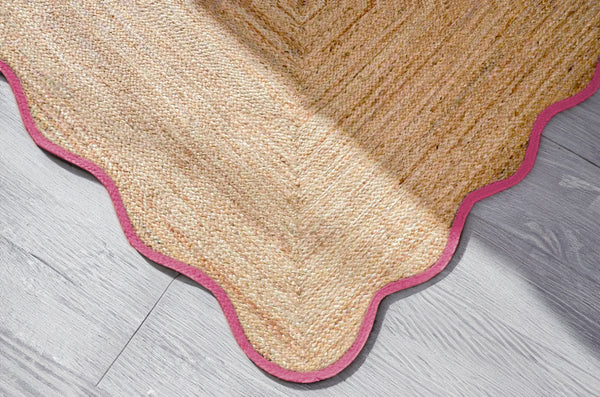 Handwoven natural jute scalloped area rug with elegant pink border for modern boho living room decor.