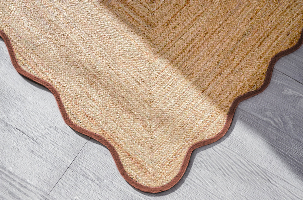Handwoven natural jute scalloped area rug with terracotta border placed in a modern living room featuring eco-friendly artisan craftsmanship.