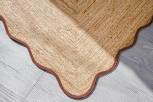 Handwoven natural jute scalloped area rug with terracotta border placed in a modern living room featuring eco-friendly artisan craftsmanship.