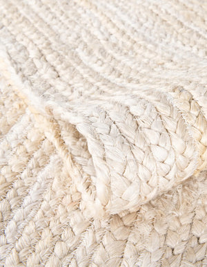 "Handwoven cream and natural jute runner rug laid on a light oak wooden floor in a brightly lit room next to a wooden bench and potted fiddle leaf fig plant."