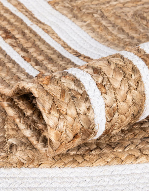 Natural woven jute rug with a navy blue double-border design, styled on a rustic wooden floor beside a wooden bench, striped throw blanket, and green potted fern.