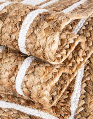 Natural jute area rug with white geometric border and braided texture styled in a warm farmhouse entryway with wooden flooring