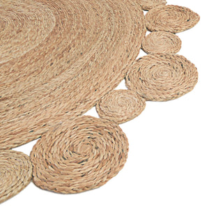Handwoven round natural jute rug with a circular scalloped border on light wood floors next to a cream armchair