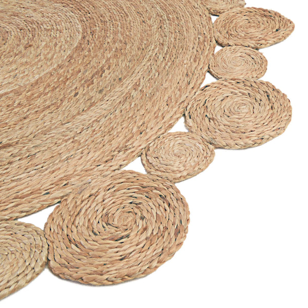 Handwoven round natural jute rug with a circular scalloped border on light wood floors next to a cream armchair
