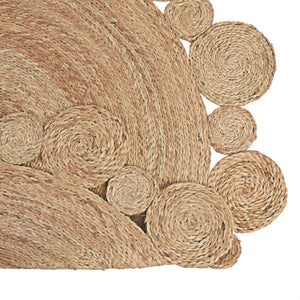 Handwoven round natural jute rug with a circular scalloped border on light wood floors next to a cream armchair