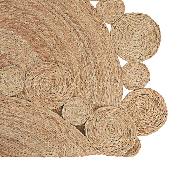 Handwoven round natural jute rug with a circular scalloped border on light wood floors next to a cream armchair