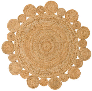 Handwoven round natural jute rug with a circular scalloped border on light wood floors next to a cream armchair