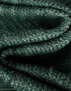 Deep green handwoven braided jute runner rug placed on a hardwood floor alongside a wooden bench in an entryway.