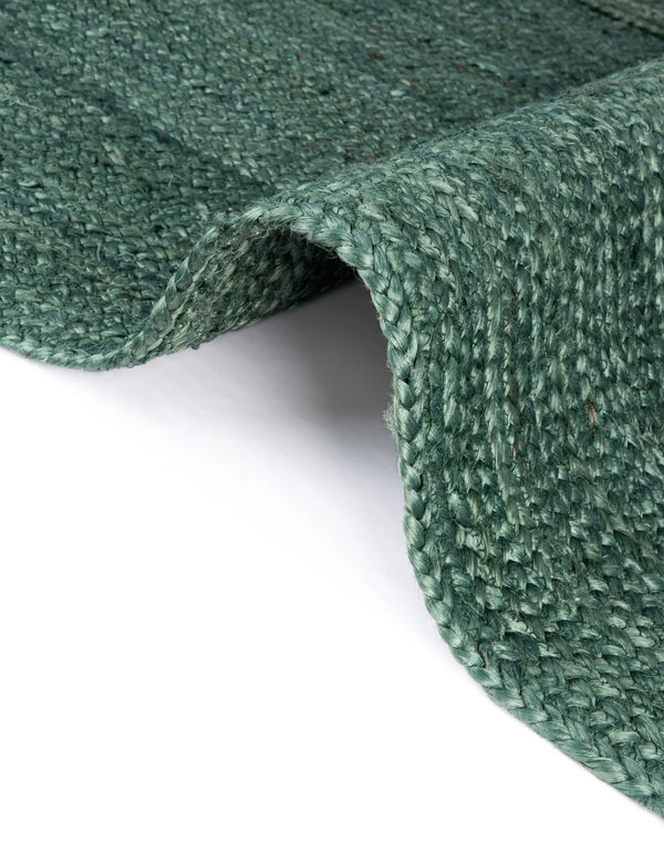Deep green handwoven braided jute runner rug placed on a hardwood floor alongside a wooden bench in an entryway.