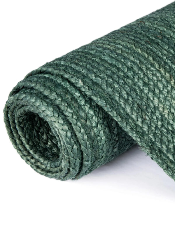 Deep green handwoven braided jute runner rug placed on a hardwood floor alongside a wooden bench in an entryway.