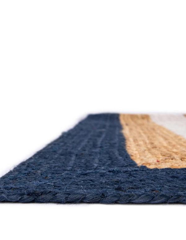 Handwoven natural jute area rug with ivory and navy blue borders styled in a bright coastal living room with a cream sofa and wooden furniture