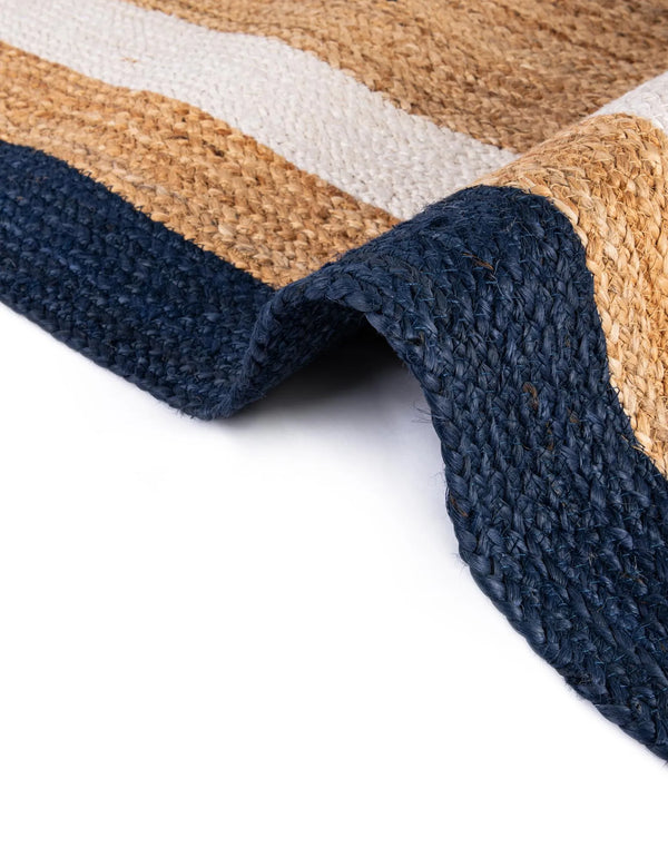 Handwoven natural jute area rug with ivory and navy blue borders styled in a bright coastal living room with a cream sofa and wooden furniture