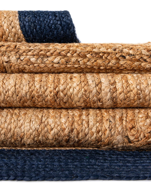 Handwoven natural jute area rug with ivory and navy blue borders styled in a bright coastal living room with a cream sofa and wooden furniture
