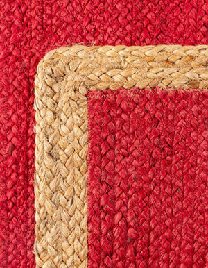 Red handwoven textured jute area rug with natural border styled on a wooden floor in a cozy rustic entryway