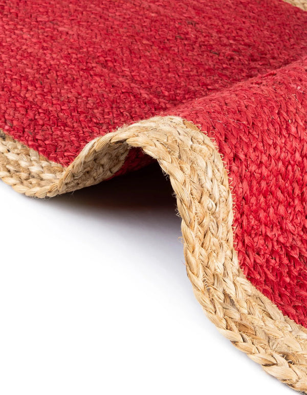 Red handwoven textured jute area rug with natural border styled on a wooden floor in a cozy rustic entryway