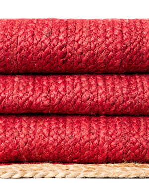 Red handwoven textured jute area rug with natural border styled on a wooden floor in a cozy rustic entryway