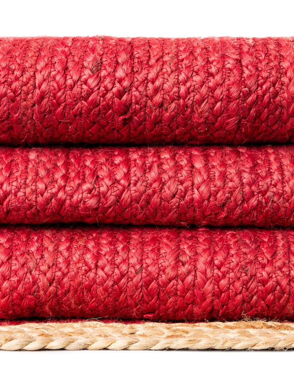 Red handwoven textured jute area rug with natural border styled on a wooden floor in a cozy rustic entryway