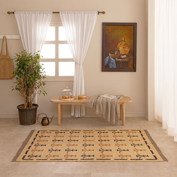 Handwoven mustard yellow and off-white geometric kilim jute rug with fringe trim, laid flat on a tile floor with a white ceramic vase and book lifestyle setting.