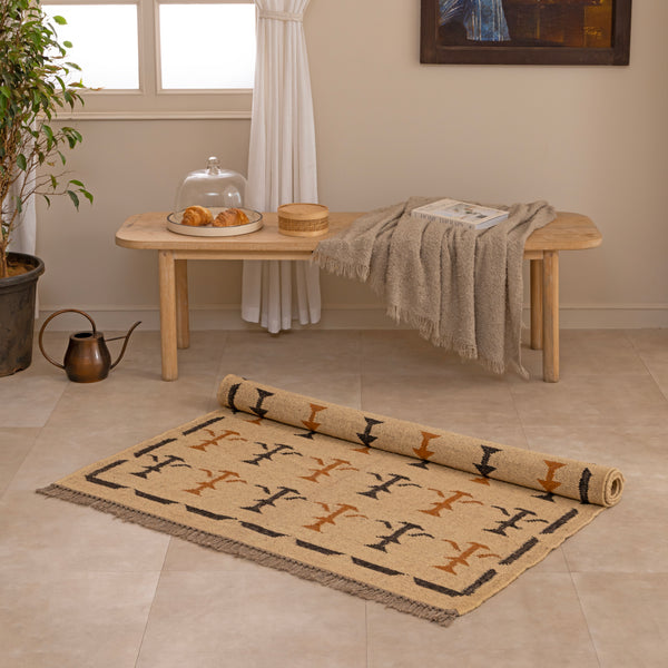 Handwoven mustard yellow and off-white geometric kilim jute rug with fringe trim, laid flat on a tile floor with a white ceramic vase and book lifestyle setting.