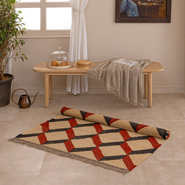 Handwoven jute and wool area rug featuring a 3D geometric optical cube pattern in terracotta rust, charcoal black, and natural beige, displayed on a tile floor with a ceramic vase and book.