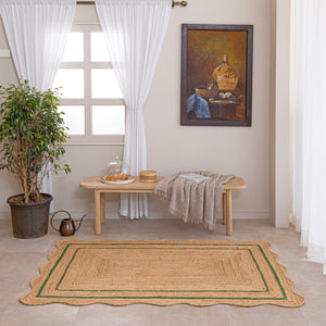 Handcrafted natural jute area rug with a double green border line and a wavy scalloped edge, displayed on a beige tile floor.