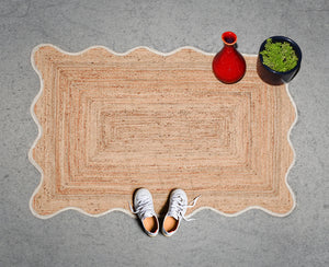 Handwoven natural jute scalloped area rug with white border placed in a modern living room featuring eco-friendly braided craftsmanship.