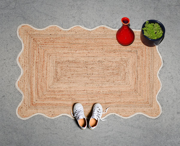 Handwoven natural jute scalloped area rug with white border placed in a modern living room featuring eco-friendly braided craftsmanship.