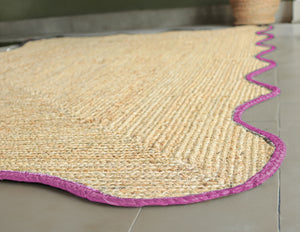 Handwoven natural jute scalloped area rug with elegant pink border for modern boho living room decor.