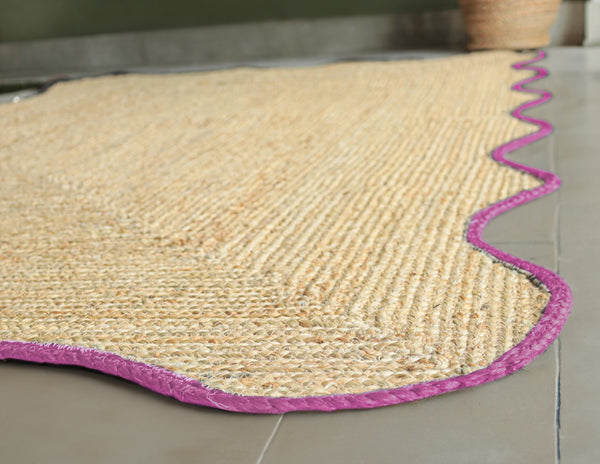 Handwoven natural jute scalloped area rug with elegant pink border for modern boho living room decor.