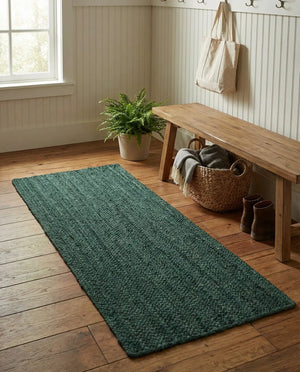 Deep green handwoven braided jute runner rug placed on a hardwood floor alongside a wooden bench in an entryway.