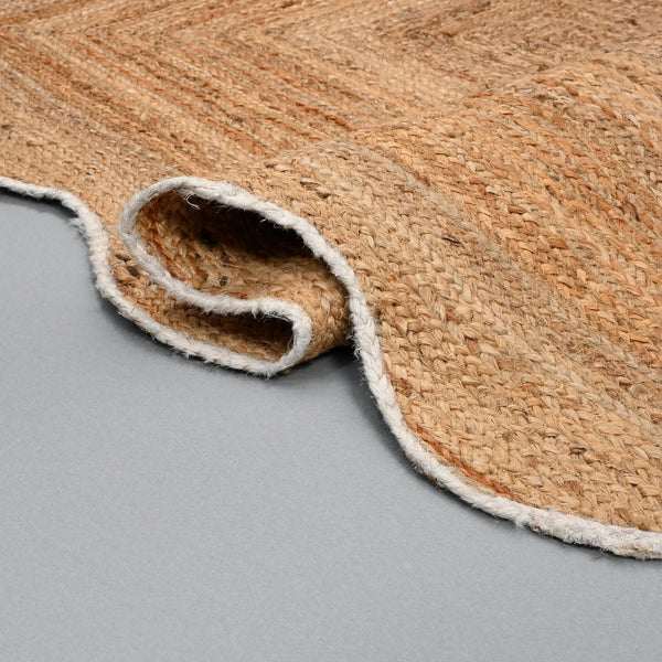 Handwoven natural jute scalloped area rug with white border placed in a modern living room featuring eco-friendly braided craftsmanship.