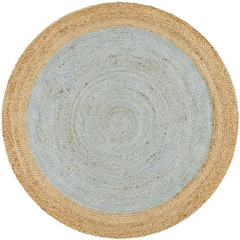 A high-angle view of a modern living room featuring a round braided jute area rug with a pastel light blue center and a natural tan border, styled on light hardwood floors with a cream sofa and a wooden armchair.