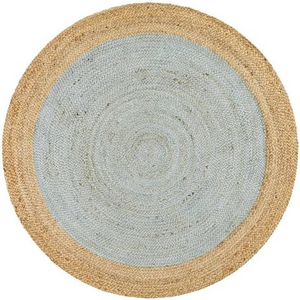 A high-angle view of a modern living room featuring a round braided jute area rug with a pastel light blue center and a natural tan border, styled on light hardwood floors with a cream sofa and a wooden armchair.
