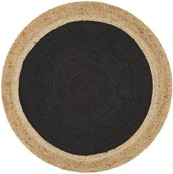 A high-angle view of a modern living room featuring a round braided jute area rug with a large charcoal black center and a natural tan border, placed on light hardwood flooring in front of a beige sofa and wooden armchair.