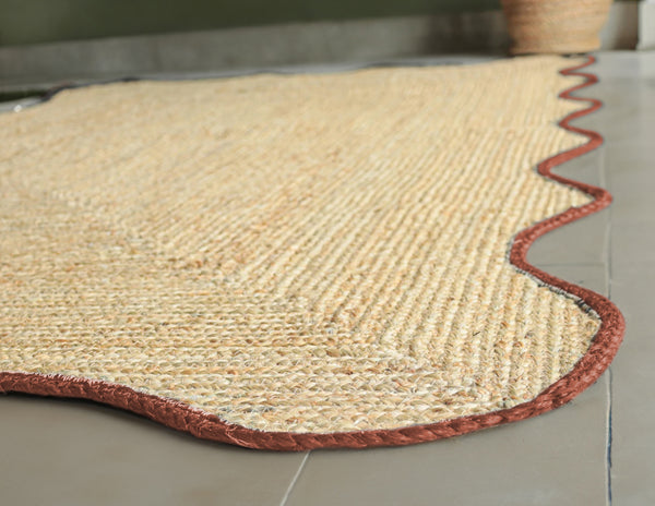 Handwoven natural jute scalloped area rug with terracotta border placed in a modern living room featuring eco-friendly artisan craftsmanship.