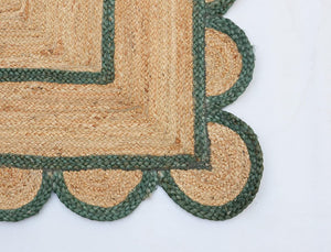 Handwoven natural jute scalloped area rug with sage green border styled in a modern Scandinavian living room.