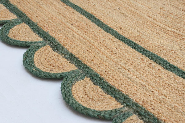 Handwoven natural jute scalloped area rug with sage green border styled in a modern Scandinavian living room.