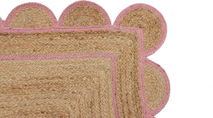 Handwoven natural jute area rug with a soft pink scalloped border styled in a modern Scandinavian living room featuring neutral furniture and natural wood flooring.