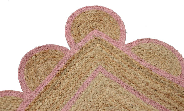 Handwoven natural jute area rug with a soft pink scalloped border styled in a modern Scandinavian living room featuring neutral furniture and natural wood flooring.