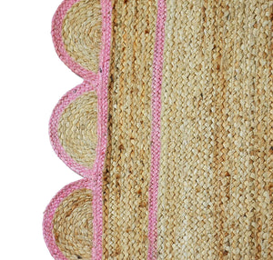 Handwoven natural jute area rug with a soft pink scalloped border styled in a modern Scandinavian living room featuring neutral furniture and natural wood flooring.