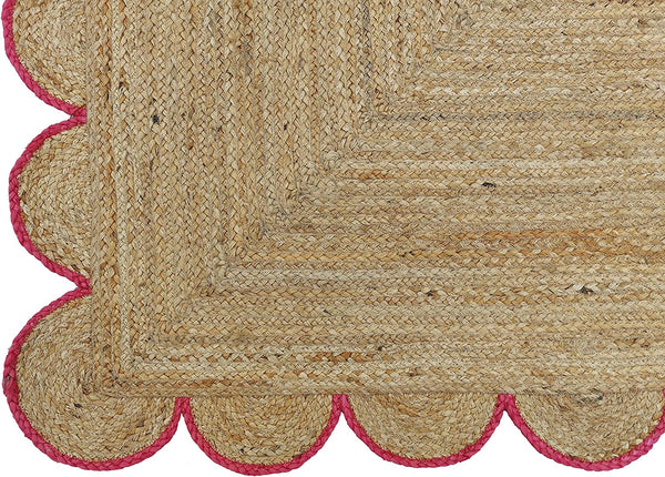 Handwoven natural jute area rug with pink scalloped border in a modern Scandinavian living room.