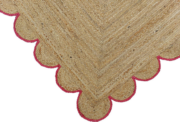 Handwoven natural jute area rug with pink scalloped border in a modern Scandinavian living room.