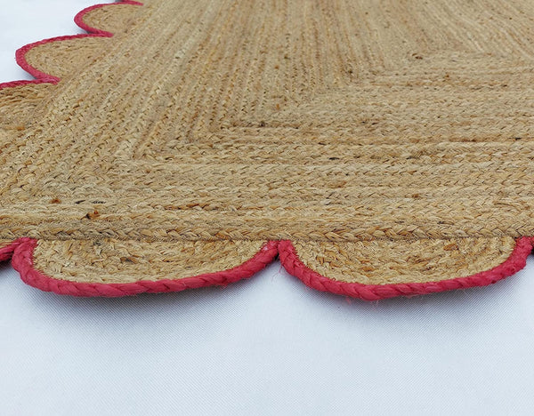 Handwoven natural jute area rug with pink scalloped border in a modern Scandinavian living room.