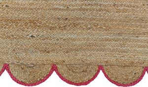 Handwoven natural jute area rug with pink scalloped border in a modern Scandinavian living room.