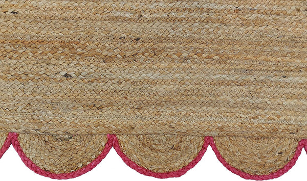 Handwoven natural jute area rug with pink scalloped border in a modern Scandinavian living room.
