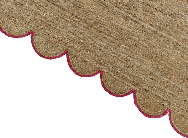 Handwoven natural jute area rug with pink scalloped border in a modern Scandinavian living room.