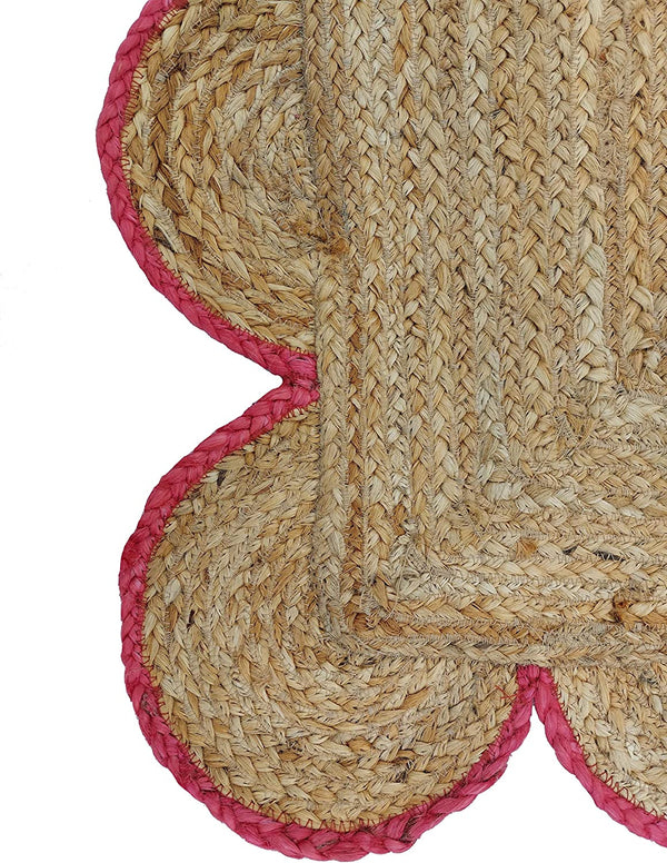 Handwoven natural jute area rug with pink scalloped border in a modern Scandinavian living room.
