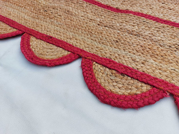 Handwoven natural jute area rug with bold red scalloped border and braided rectangular design