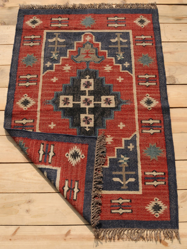 Handwoven red and navy blue tribal wool area rug with geometric Southwestern pattern and fringe, displayed on a natural wooden floor.